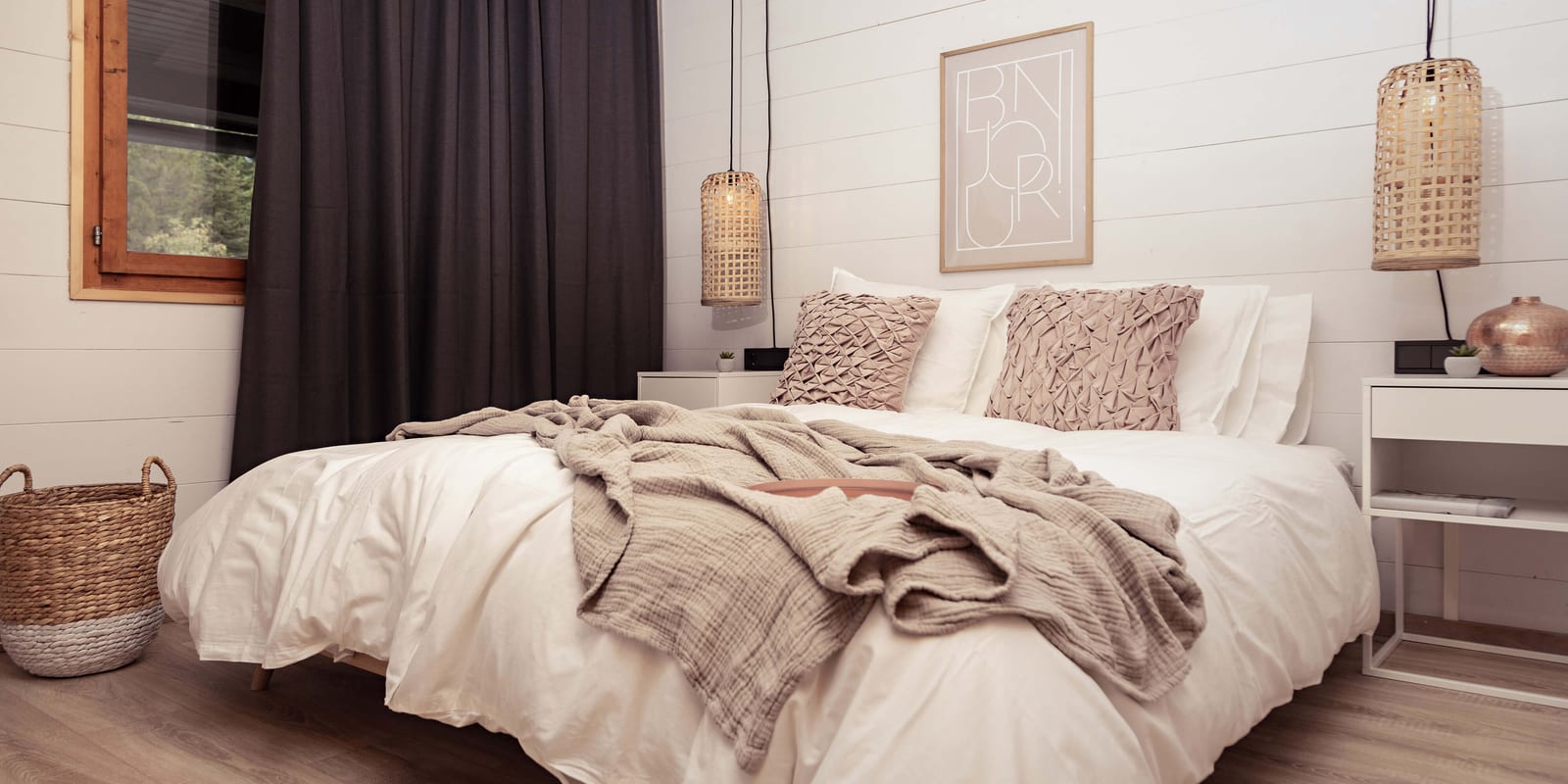 Schlafzimmer in Apartment Frieda mit Doppelbett, Leinenwäsche, Rattanleuchten und dunklem Vorhang.