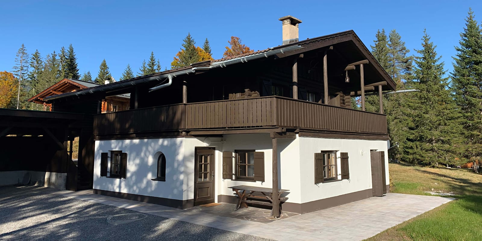 Das Chalet Franz im Spätsommer, Vorderansicht mit Balkon, Carport und herbstlich gefärbten Bäumen.
