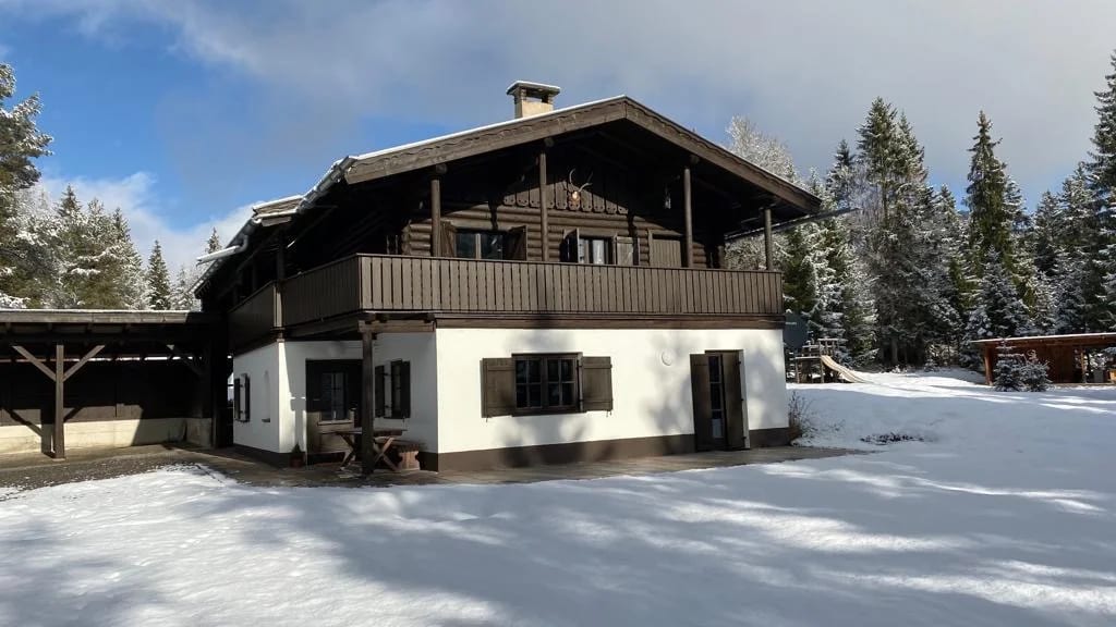 Das Chalet Franz im Schnee, davor eine unberührte Schneefläche, dahinter verschneite Fichten und blauer Himmel.