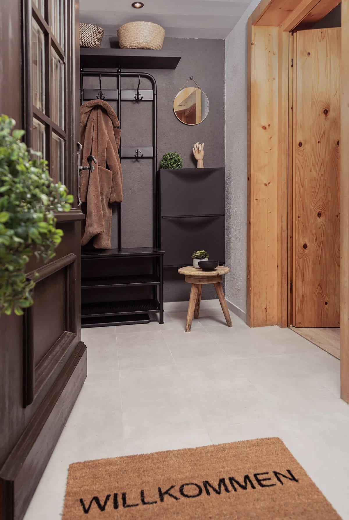 Eingangsbereich von Apartment Xaver mit Garderobe, Holztür und Fußmatte mit der Aufschrift Willkommen.